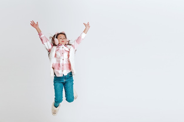 Bambina felice in vestiti caldi che salta su uno sfondo bianco Spazio per il testo