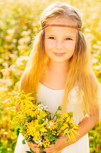 Bambina felice su un prato estivo in natura tiene un bouquet con fiori gialli e sorrisi