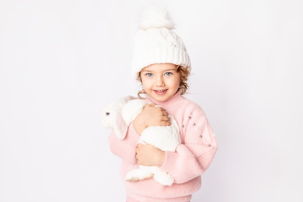 Bambina felice su uno sfondo bianco isolato con un coniglietto di Natale nelle sue mani in un maglione rosa e cappello sorridente spazio per il testo