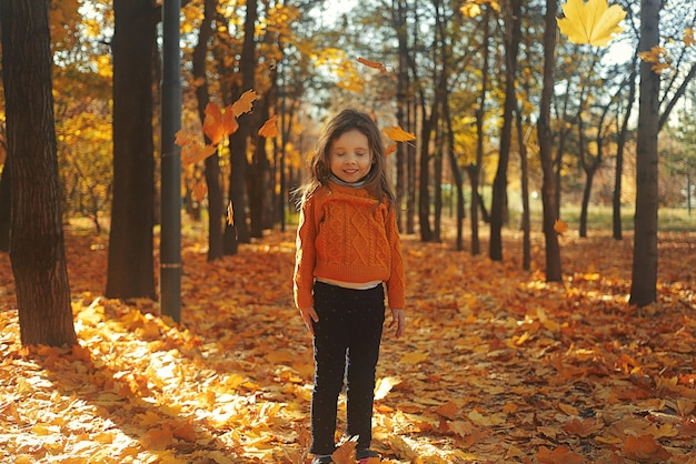 Bambina felice sveglia che gioca con le foglie cadute nel parco di autunno di mattina