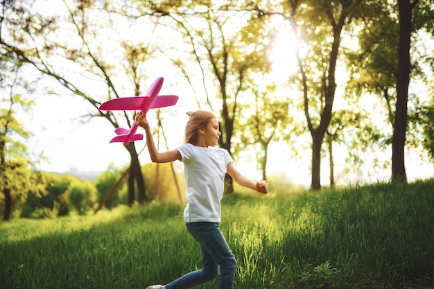 Bambina, gioca con un aereo giocattolo in aria nel parco.