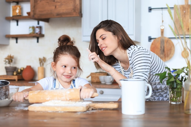 Bambina giocosa che cucina in cucina con sua madre amorevole.