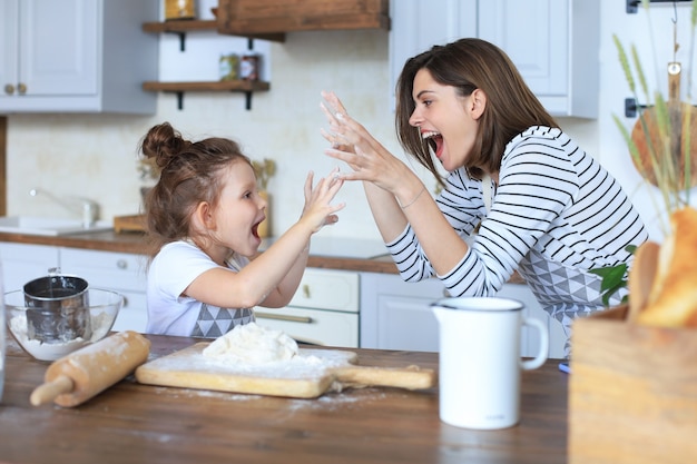 Bambina giocosa che cucina in cucina con sua madre amorevole.