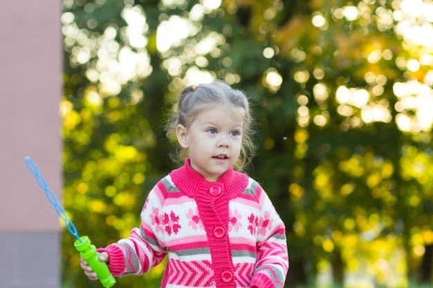 Bambina gioiosa con il giocattolo della bolla di sapone nel parco estivo e che guarda da parte