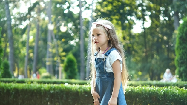 Bambina graziosa che cammina all'aperto nel parco estivo verde.