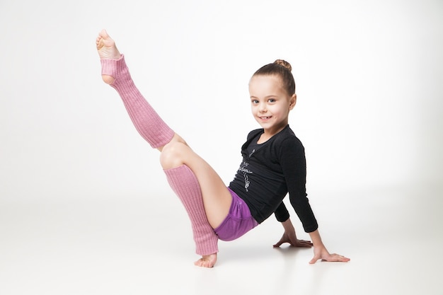 Bambina graziosa che fa ginnastica sopra fondo bianco