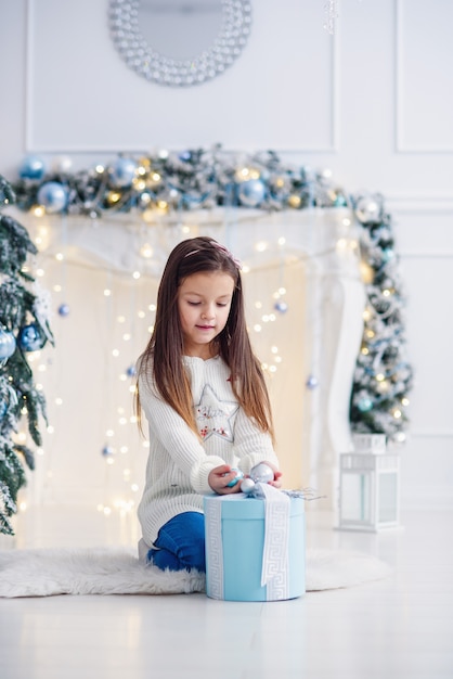 Bambina graziosa che si siede vicino all'albero di Natale all'interno.