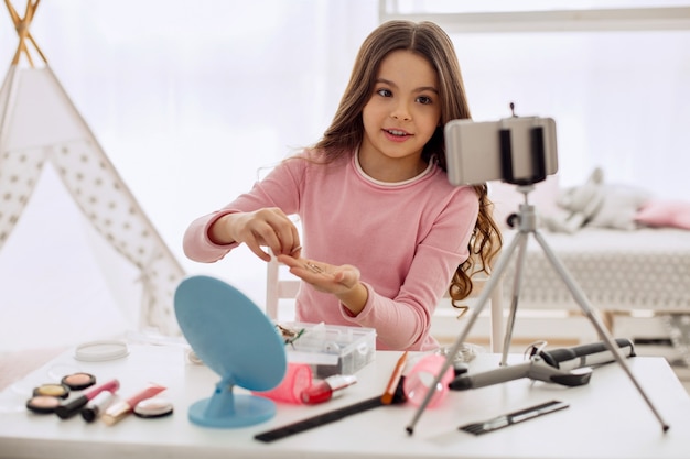 Bambina graziosa che spazzola i suoi capelli davanti alla macchina fotografica