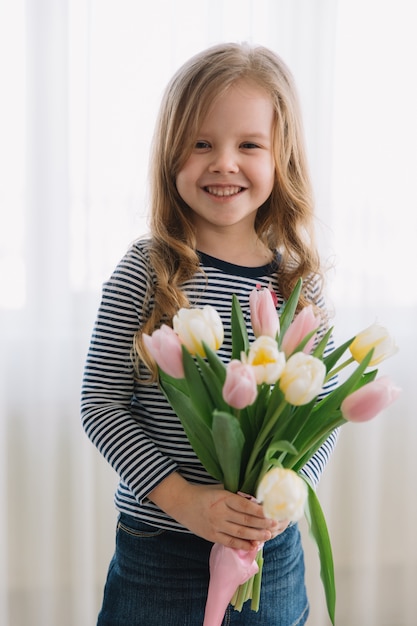 Bambina graziosa con il mazzo di tulipani su un giorno di madri felice. Fa un regalo per sua madre.