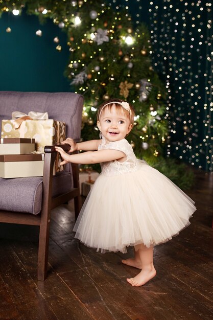 Bambina graziosa in vestito bianco che gioca e che è felice circa le luci di natale