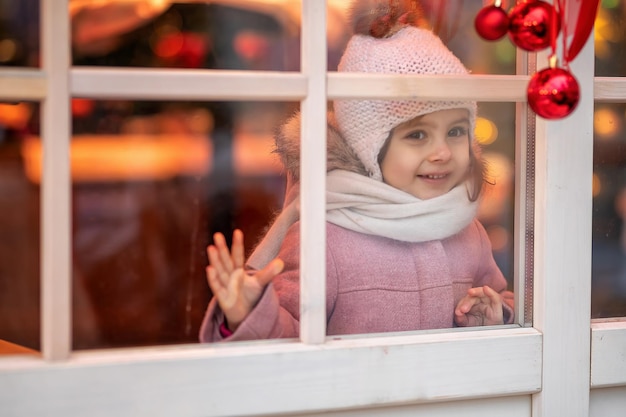 Bambina guarda fuori dalla finestra e attende i regali di Natale e di Natale Visto attraverso la finestra