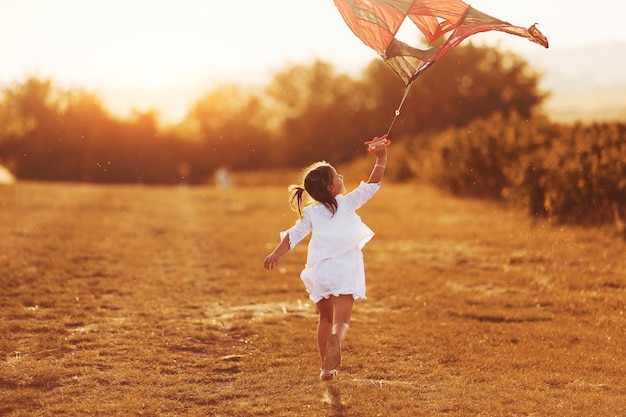 Bambina in abiti bianchi che corre con l'aquilone all'aperto sul campo