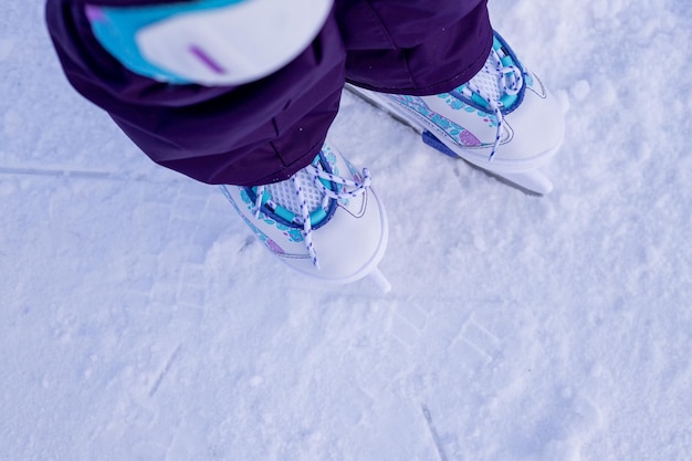 Bambina in abiti invernali con protezioni che pattinano sulla pista di pattinaggio imparando la prima lezione sulle attività invernali sul ghiaccio