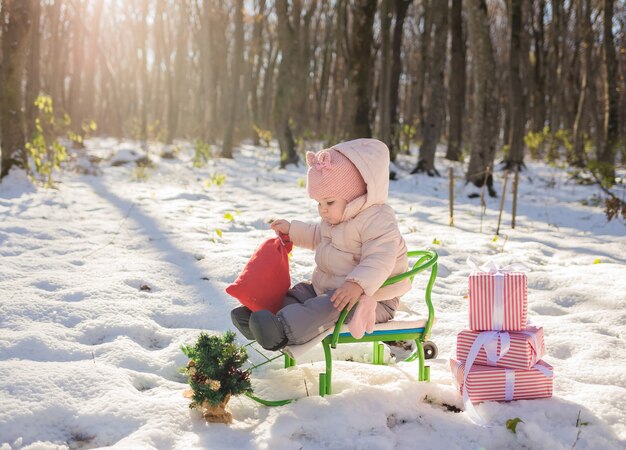 Bambina in abiti invernali seduto in una slitta con doni nella foresta invernale