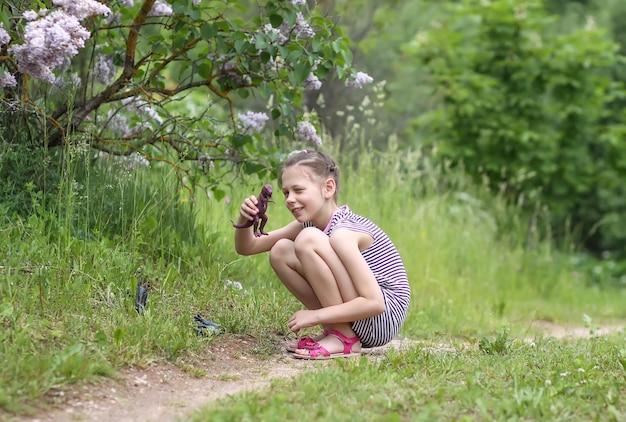 Bambina in abito a righe che gioca con il giocattolo di plastica del dinosauro nel parco di primavera