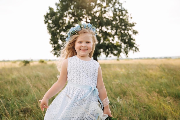 Bambina in abito azzurro cielo con corona e bouquet stare in campo davanti al grande albero