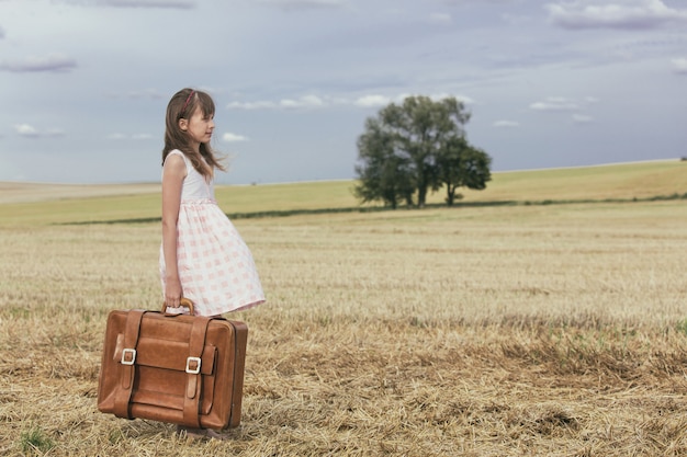 Bambina in abito classico con valigia da viaggio