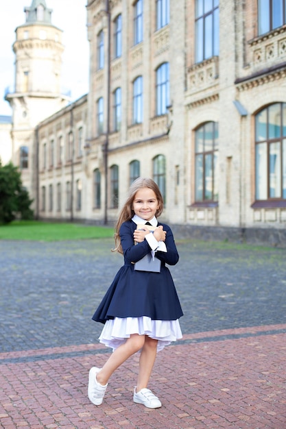 Bambina in abito e con i capelli lunghi all'aperto vicino all'edificio scolastico. Bambino con i libri.