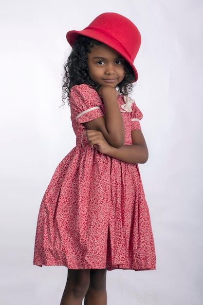 Bambina in abito fiorito con cappello rosso in studio fotografico con sfondo bianco per il ritaglio