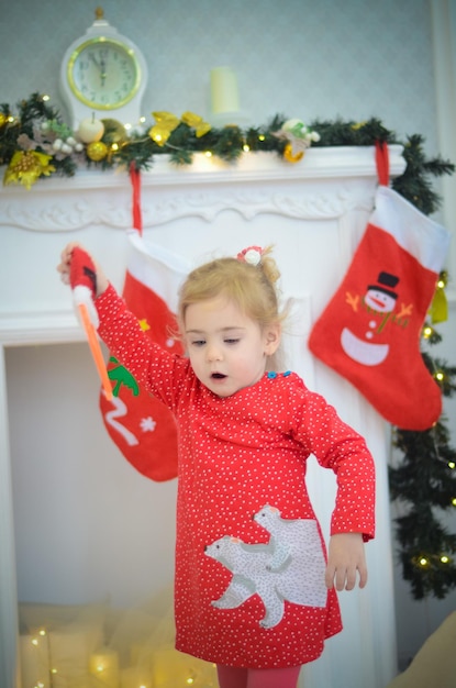 Bambina in abito rosso che gioca nella stanza con decorazioni natalizie