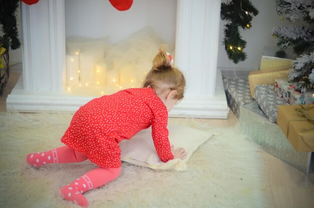 Bambina in abito rosso che gioca nella stanza con decorazioni natalizie