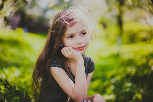 Bambina in abito scuro con capelli lunghi seduti nel giardino primaverile