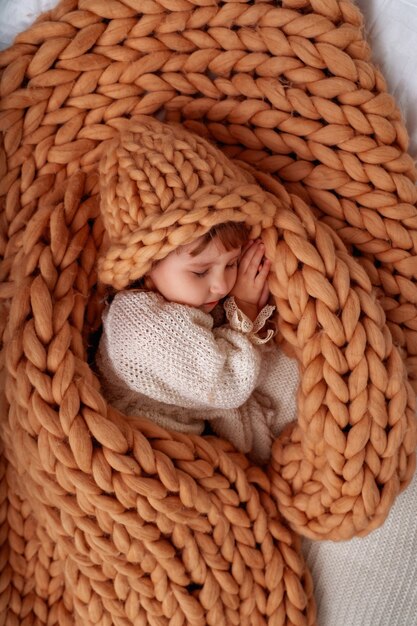 Bambina in berretto sotto coperta in lana di pecora naturale.