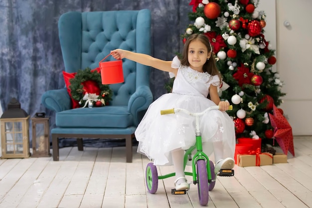 Bambina in bicicletta con un regalo di Natale sullo sfondo dell'albero di Natale