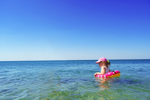 Bambina in bikini che nuota nel mare con il cerchio di nuoto da solo