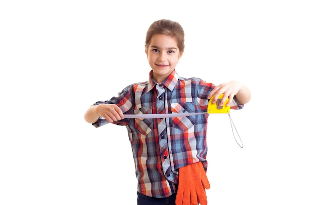 Bambina in camicia rossa a quadri con guanti arancioni e occhiali che tengono cacciavite e roulette