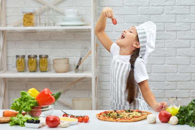 Bambina in cappello da chef e un grembiule che cucina la pizza