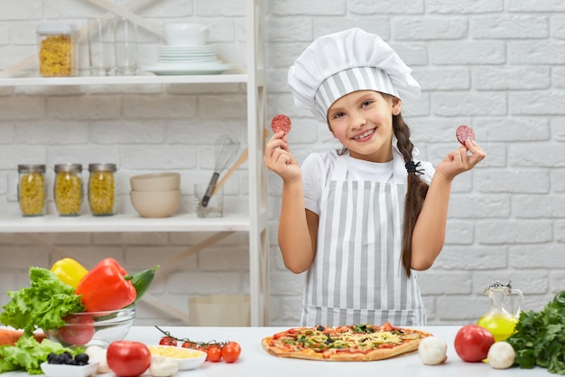 Bambina in cappello da chef e un grembiule che cucina la pizza