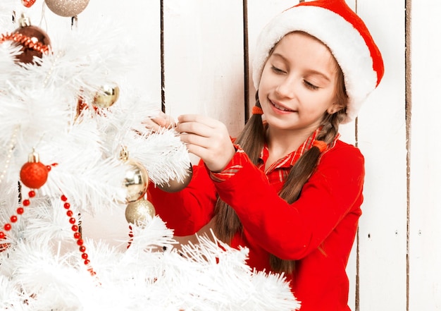 Bambina in cappello rosso della santa che decora l'albero di nuovo anno