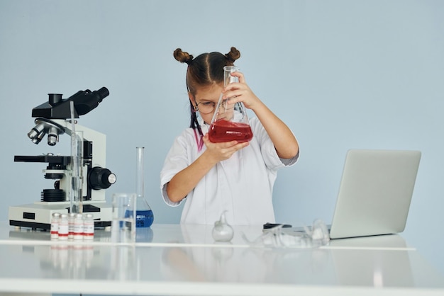 Bambina in cappotto che interpreta uno scienziato in laboratorio utilizzando attrezzature