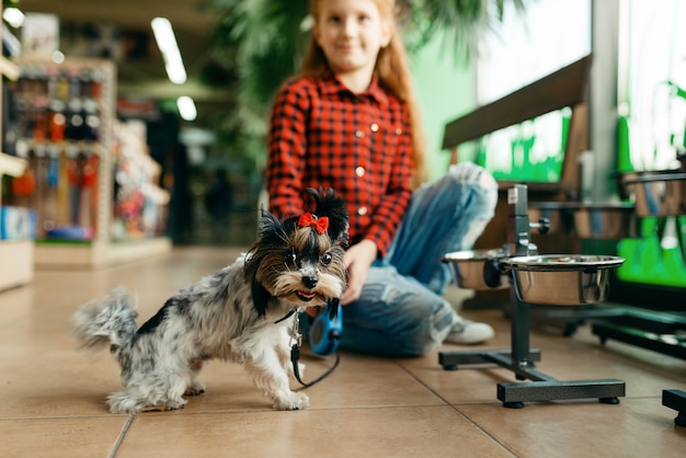 Bambina in cerca di vestiti per il suo cane in un negozio di animali. Bambino che acquista attrezzature nel negozio di animali, accessori per animali domestici