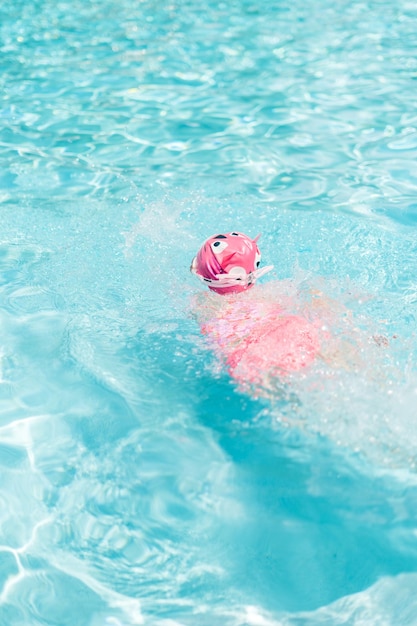 Bambina in coppa rosa da bagno e occhiali che nuotano nella piscina all'aperto in estate.