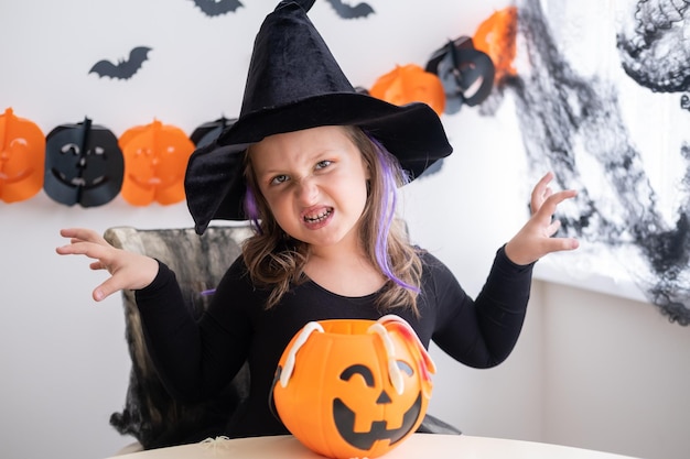 bambina in costume da strega che tiene jack zucca con caramelle, festeggia Halloween a casa