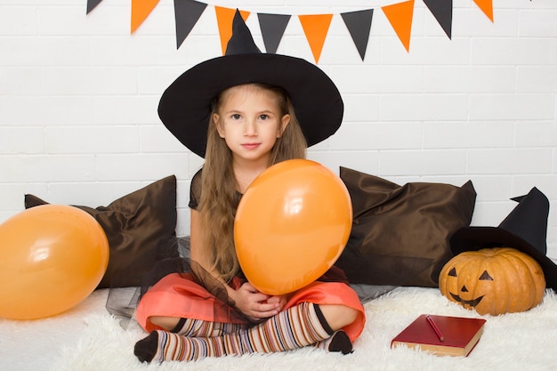 Bambina in costume da strega con un palloncino in mano che celebra halloween a casa