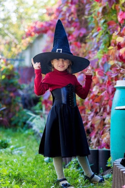 Bambina in costume da strega in posa sulla festa di halloween in giardino.