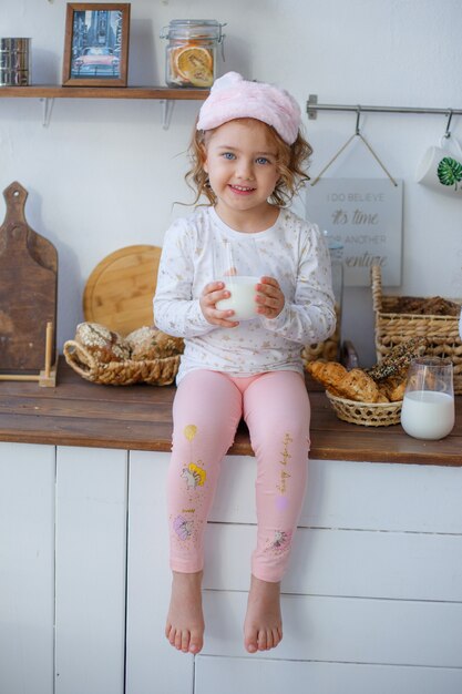 Bambina in cucina con in mano un bicchiere di latte dopo aver dormito, colazione