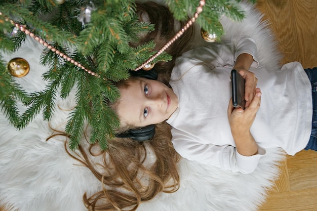 bambina in cuffia con uno smartphone giace all'albero di Natale