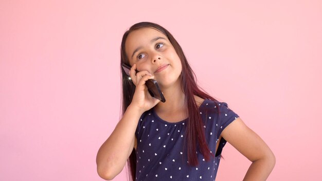 Bambina in età prescolare in un vestito che tiene un telefono cellulare, isolata sopra il rosa