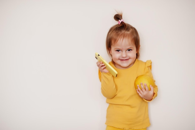 Bambina in giallo con limone e telefono cellulare, sfondo isolato.