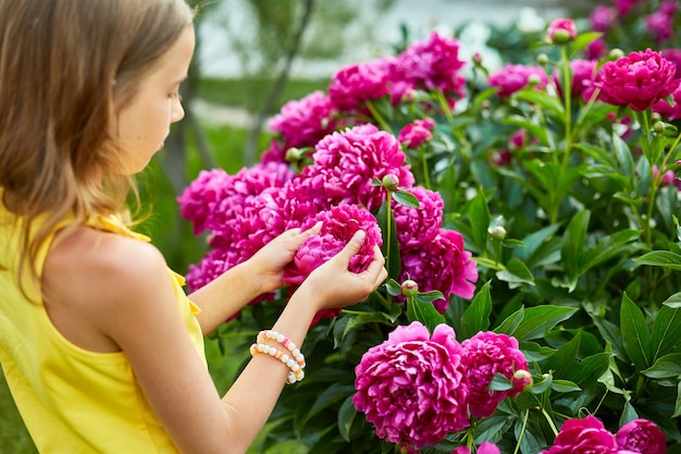 Bambina in giardino in cespugli di peonie bambino tocca il fiore