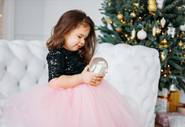 Bambina in gonna tutu bellissimo vestito con palla di vetro in salotto su di un albero di Natale