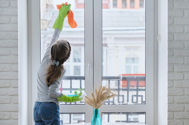 Bambina in guanti con detergente spray con finestre di pulizia straccio