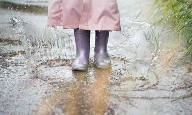 Bambina in impermeabile rosa impermeabile stivali di gomma viola salti divertenti attraverso le pozzanghere sulla strada in una giornata piovosa Primavera autunno Divertimento per bambini dopo la pioggia Attività ricreative all'aperto