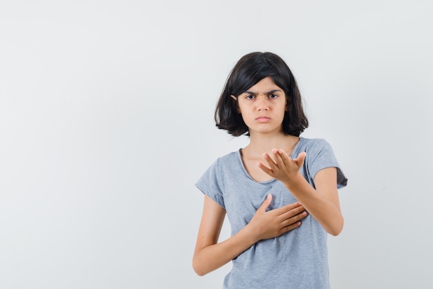 Bambina in maglietta che allunga la mano nel gesto interrogativo e che sembra serio, vista frontale.