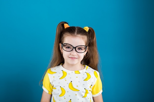 Bambina in maglietta della banana e di vetro su fondo blu