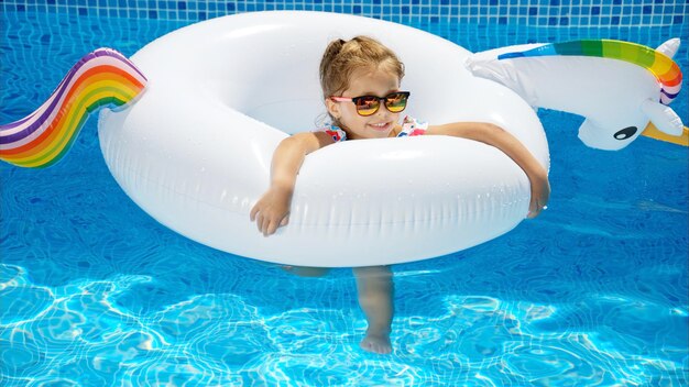 Bambina in occhiali da sole che riposa sul pallone da piscina bianco